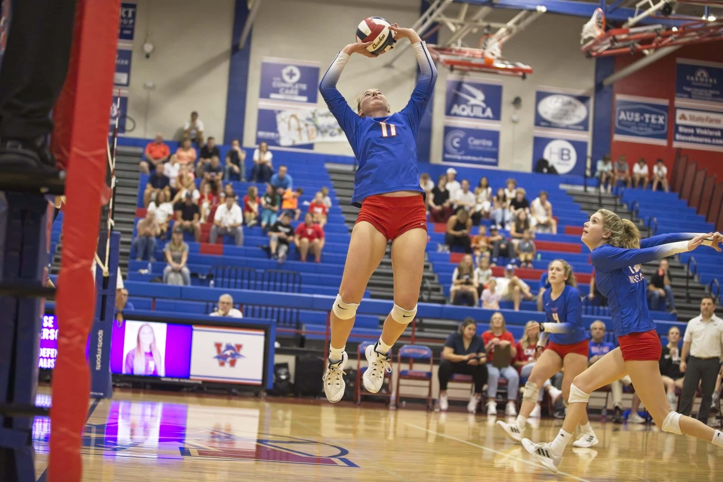 A high school volleyball player jump setting a volleyball